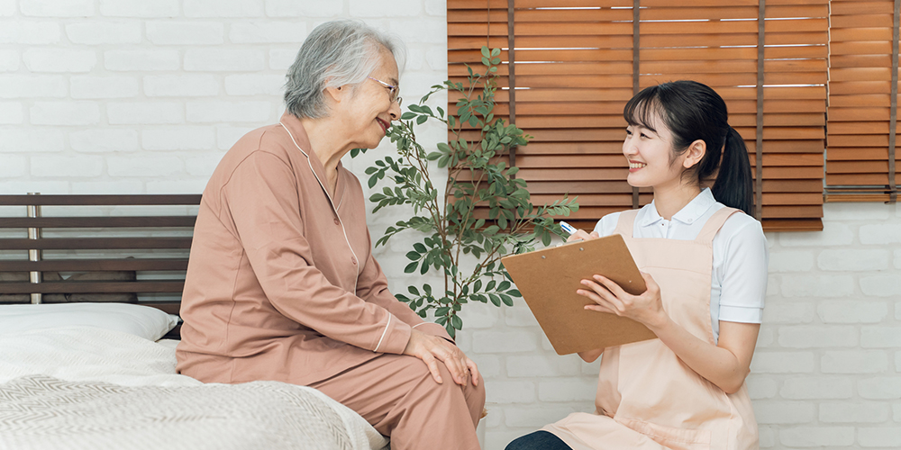 高齢女性と会話をしながらレポートに記録する介護職員